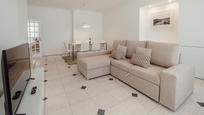 Uma sala de estar moderna com um sofá modular bege, uma mesa de jantar com cadeiras e uma televisão de tela plana.