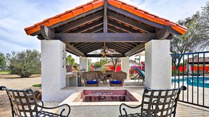 A covered outdoor seating area with two metal chairs, a wooden table, and a central fire pit. - Pool & Putting Green: Group Getaway in Glendale! (Glendale)