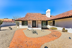 Une maison avec un toit en tuiles, un chemin en briques et des cactus dans le jardin.