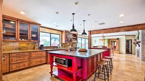 A spacious kitchen with wooden cabinets, a central island with stools, and a large window providing natural light. - Pool & Putting Green: Group Getaway in Glendale! (Glendale)