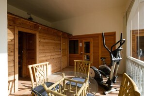 Una habitación con detalles de madera, una mesa de vidrio con sillas y equipo de ejercicio.