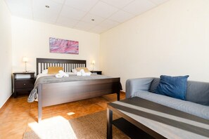 A bedroom with a bed, bedside tables, a sofa, and a painting on the wall.