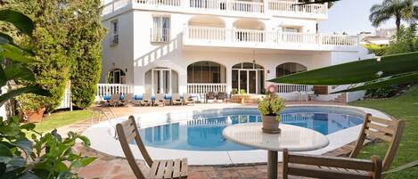 A two-story white building with a swimming pool, outdoor seating, and a well-maintained garden.