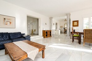 A spacious living room with a dark leather sofa, a wooden coffee table, and a dining area with wicker furniture.