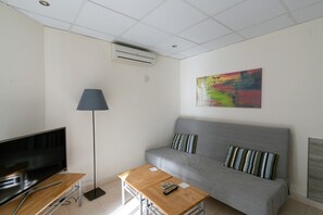 A modern living room with a flat-screen TV, a wooden coffee table, a grey sofa with striped pillows, a floor lamp, and a colorful abstract painting on the wall.