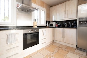 A kitchen with white cabinets, a black countertop, a stainless steel oven, a microwave, and a refrigerator.