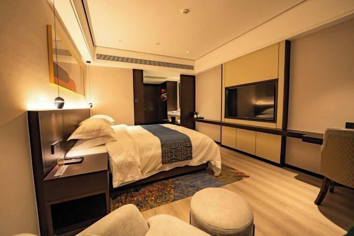 A modern hotel room with a large bed, bedside tables, a TV, and a seating area.