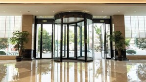 Un vestíbulo con puerta giratoria, ventanas amplias y plantas en macetas.