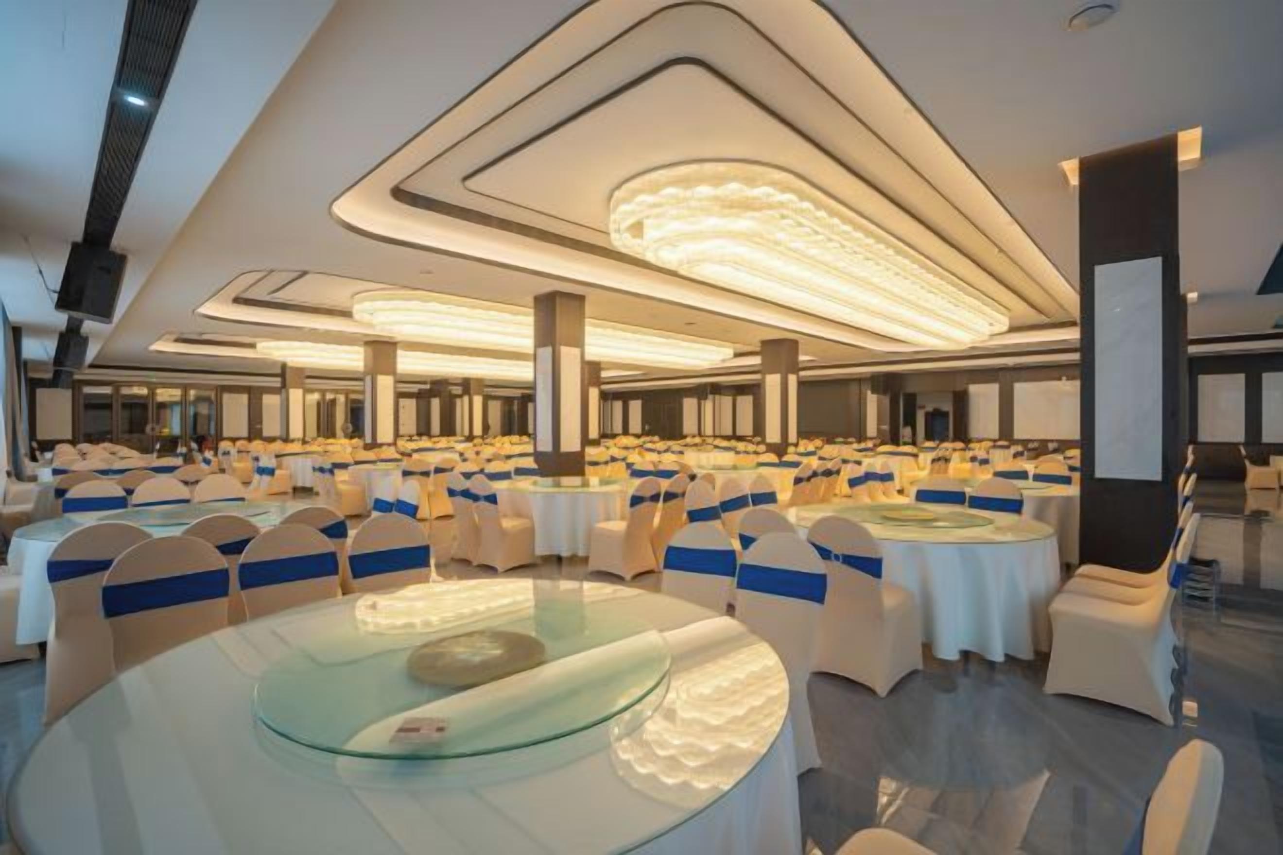 A banquet hall with round tables and chairs, large windows, and a modern ceiling design.
