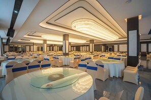 Un salón de banquetes con mesas y sillas redondas, ventanas amplias y un diseño moderno de techo.