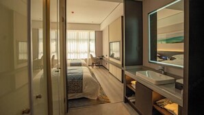 Una habitación de hotel moderna con una cama grande, una mesita de noche, un espejo y un baño con lavabo y espejo.