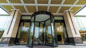 Entrada con puerta giratoria, paneles de vidrio y techo con diseño.