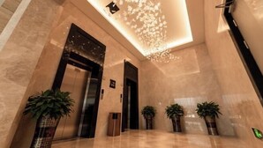 Un vestíbulo moderno con piso de mármol, un ascensor central y plantas en macetas.