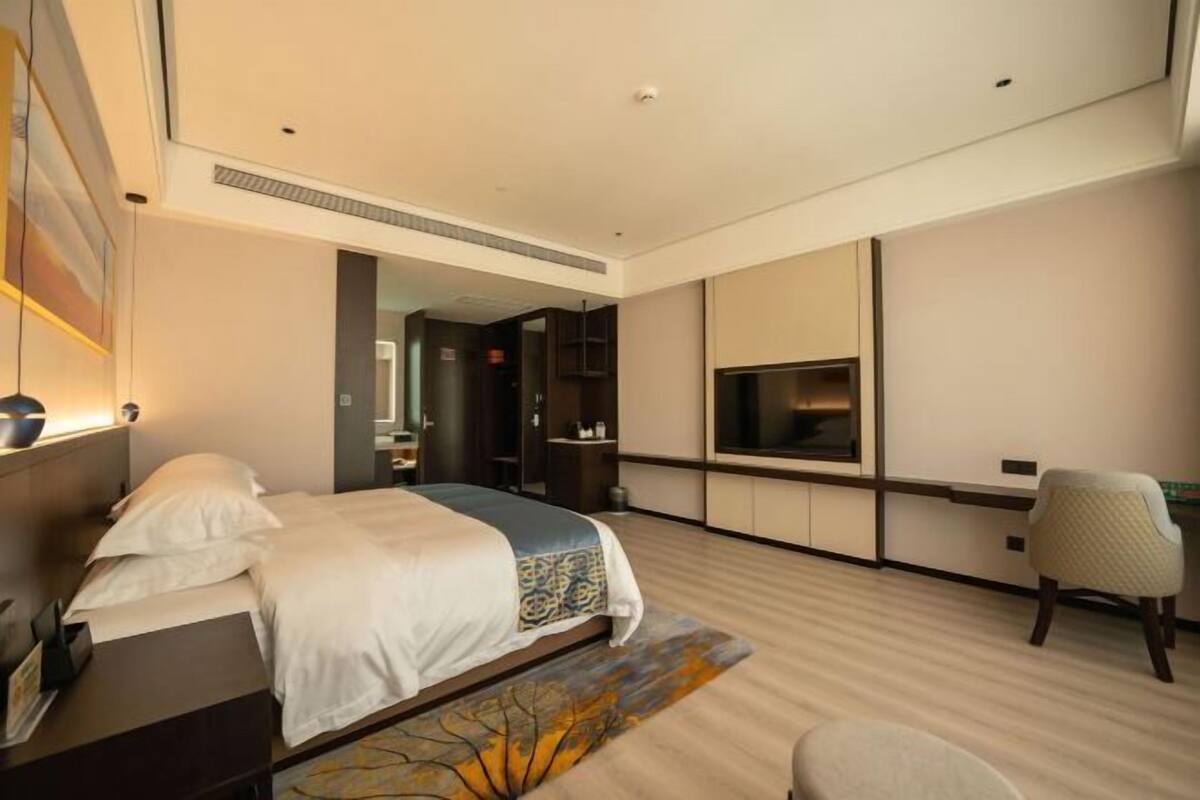 A modern hotel room with a bed, a desk, a chair, a TV, and a large mirror.