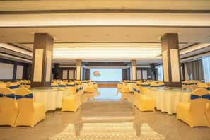 A conference room with rows of tables and chairs, a podium, and a presentation screen. - Cotton Rose Hotel (Cili)