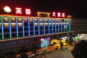 Un hotel amb un rètol destacat, diverses plantes i una zona d'aparcament.