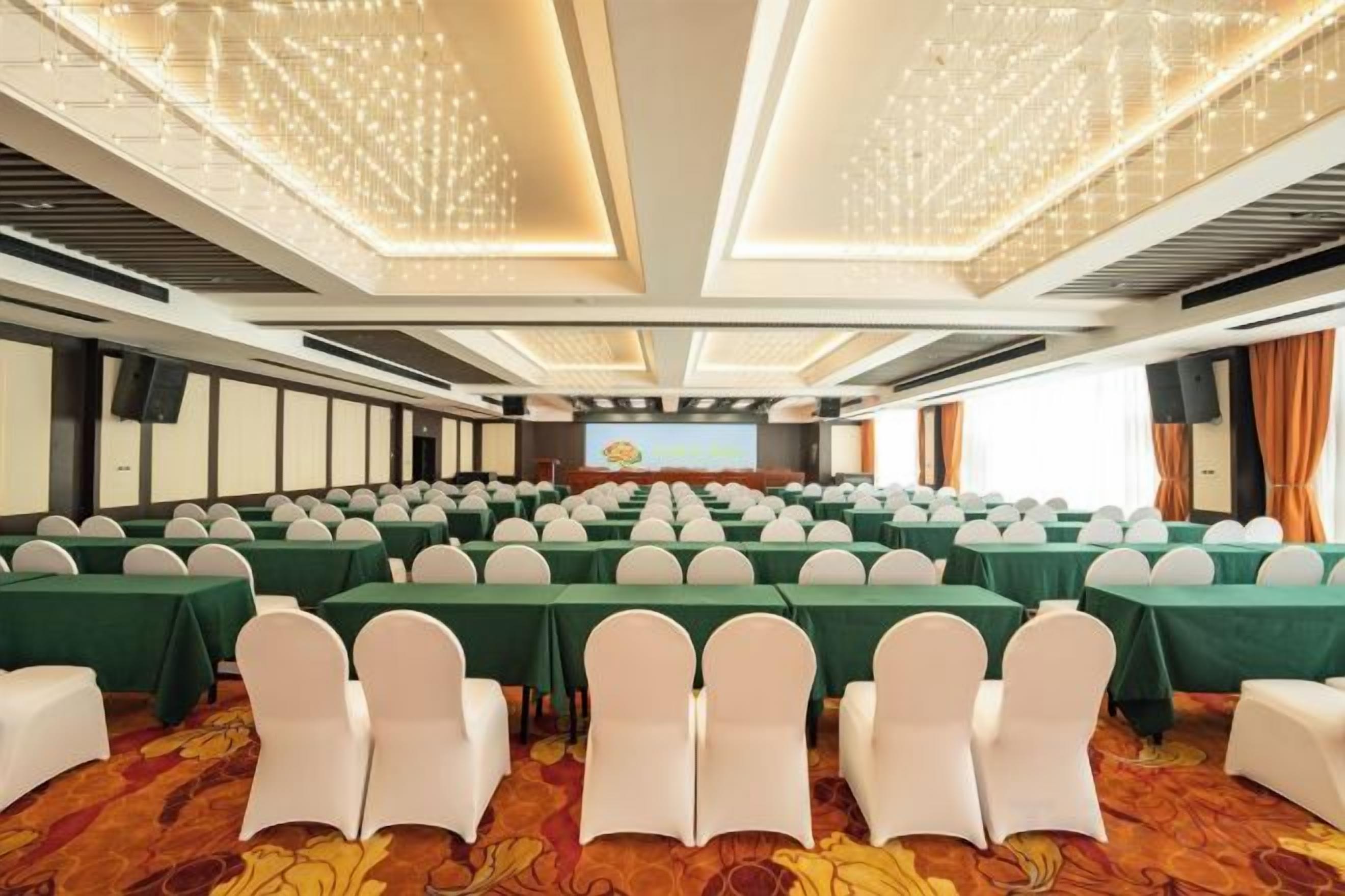 A conference room with rows of tables and chairs, a stage with a podium, and a large screen.