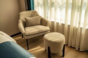Una habitación con un sillón color beige, un reposapiés a juego y una cama con almohada azul.