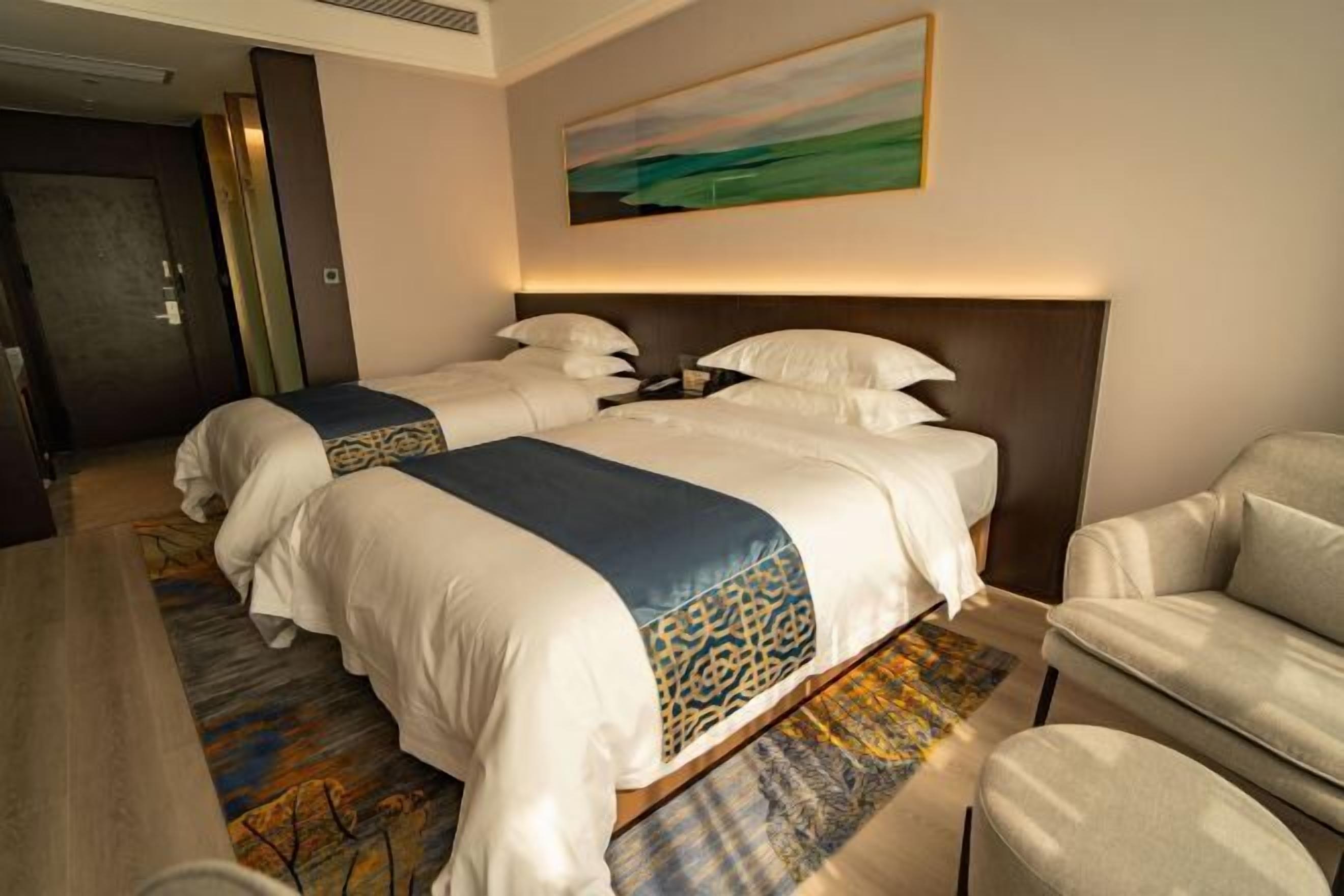 Quarto de hotel com duas camas, um sofá e um quadro na parede.