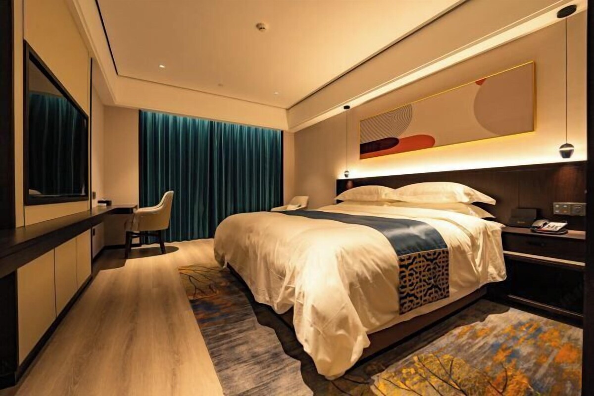Habitación de hotel moderna con una cama grande, un escritorio, una silla, un espejo y vistas a la ciudad.
