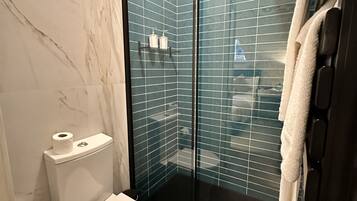 Un baño con inodoro, cabina de ducha de vidrio y un perchero para toallas.