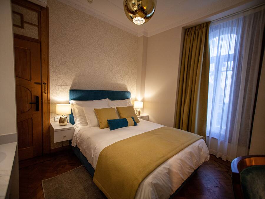 Een keurig opgemaakt slaapkamer met een bed, nachtkastjes en een raam met gordijnen.