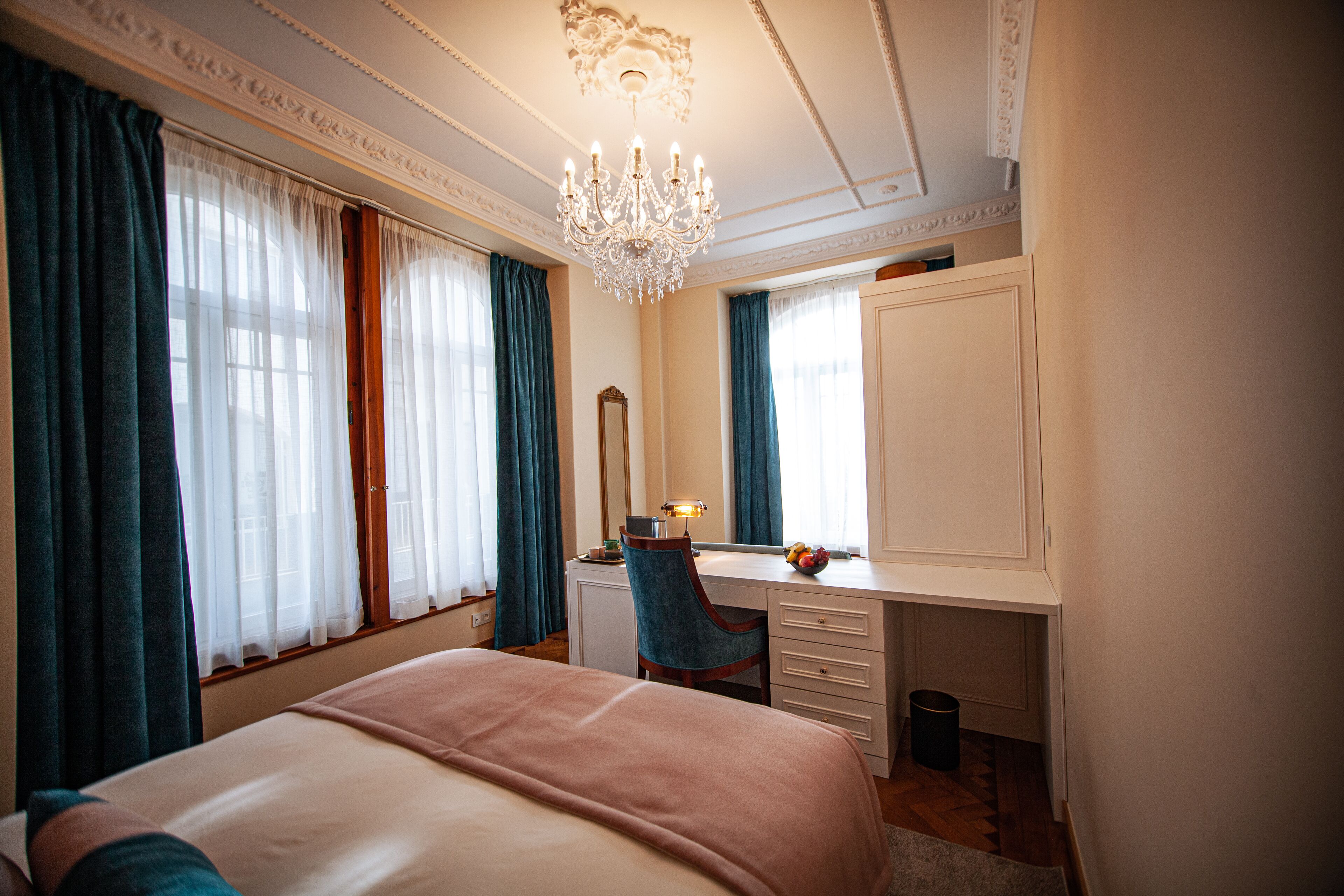 Una habitación de hotel con una cama grande, un escritorio con una silla, un espejo y una araña.
