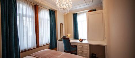 Una habitación de hotel con una cama grande, un escritorio con una silla, un espejo y una araña.