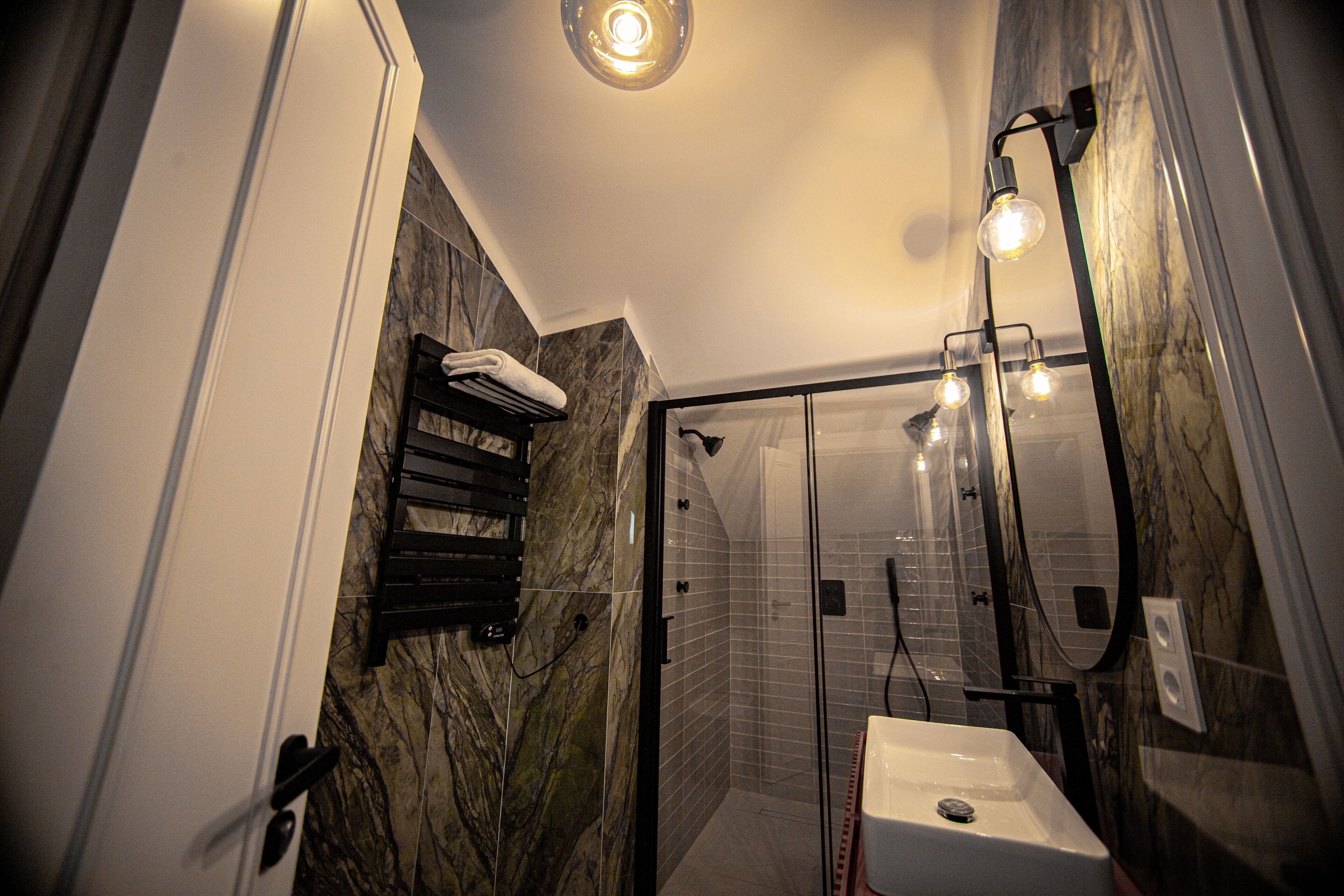 A modern bathroom with a glass shower enclosure, a marble wall, and a white sink.