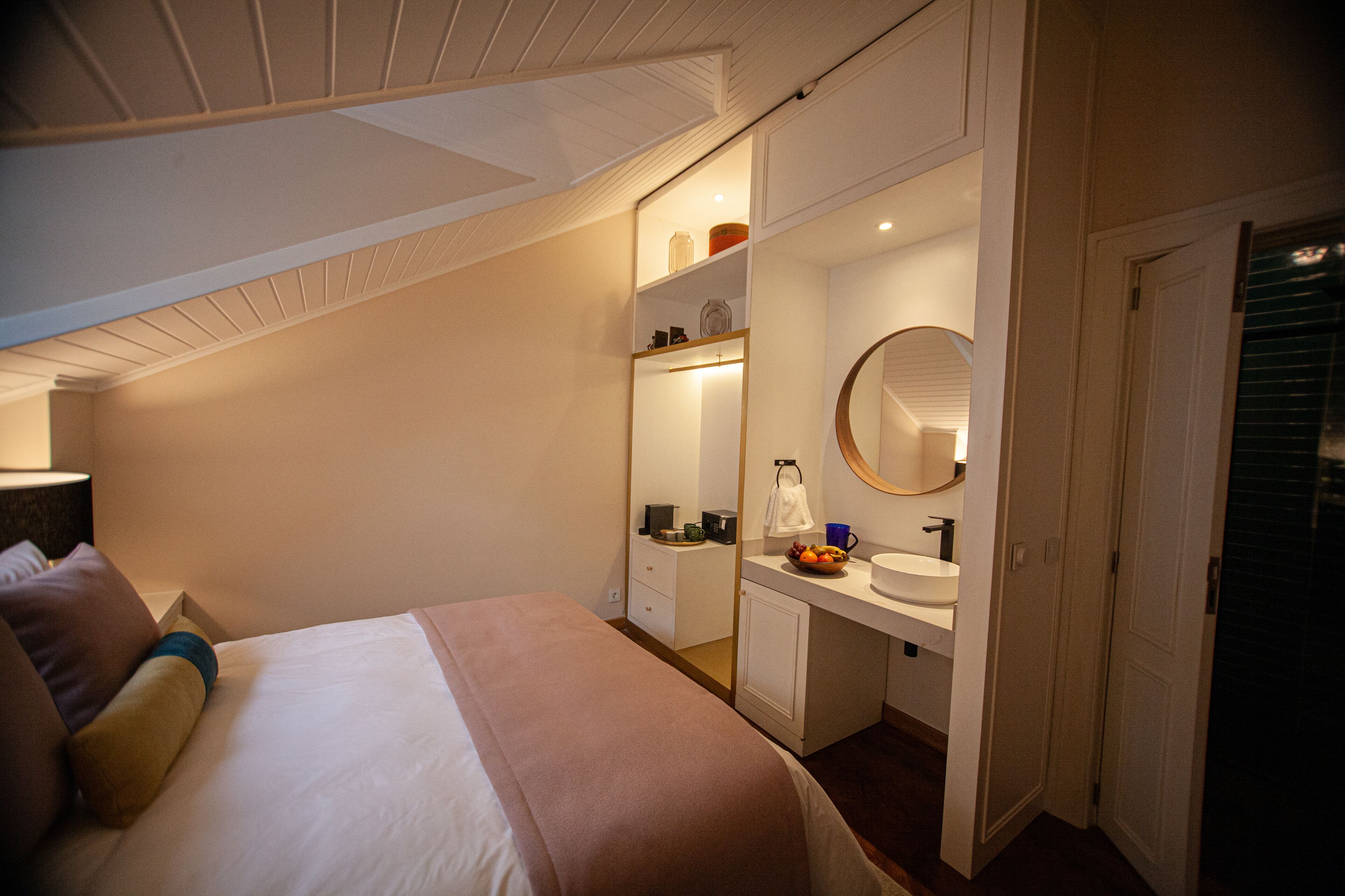 A bedroom with a bed, bedside table, and a bathroom with a sink and mirror.