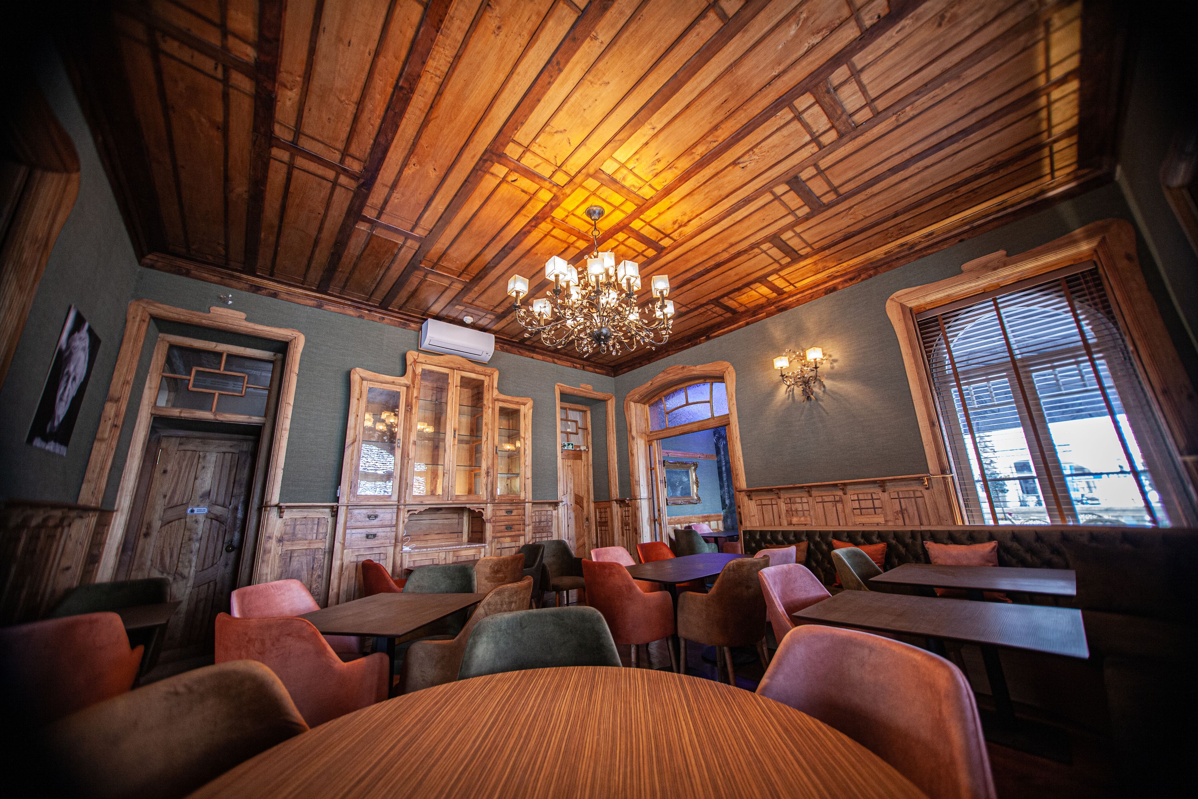 Un restaurant doté de poutres en bois au plafond, d’un lustre et de différents types de mobilier, notamment des tables et des chaises.