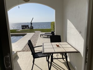 En udendørs terrasse med et bord og stole, en lille pool og havudsigt.