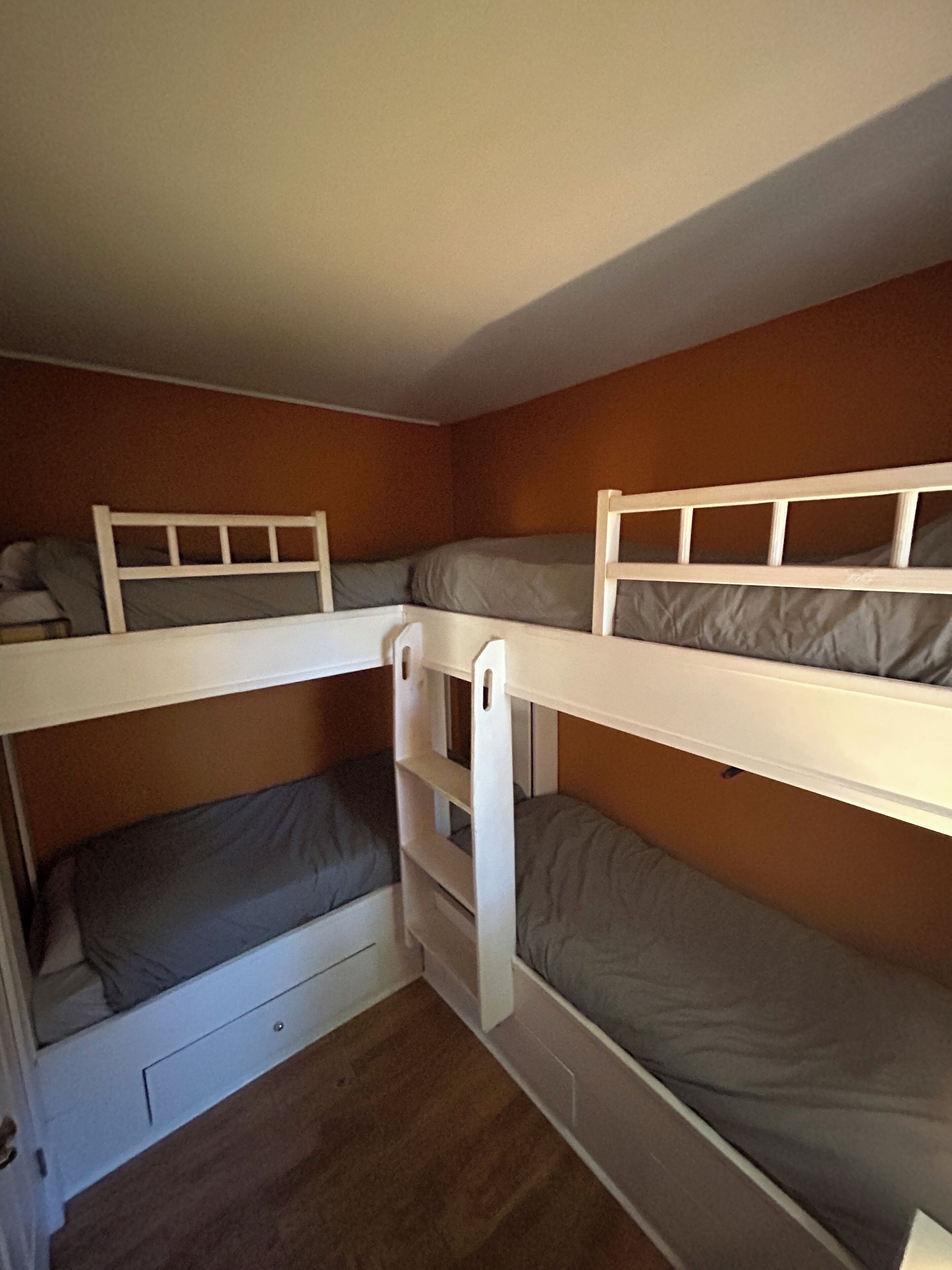 Une chambre avec un lit superposé, dont les structures sont en bois et la literie est grise.