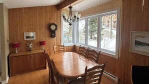 Un espace repas comprenant une table et des chaises en bois, un lustre et une grande fenêtre donnant sur l’extérieur.