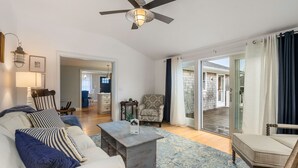 A spacious living room with a sofa, armchairs, a coffee table, and a ceiling fan. There is a sliding glass door leading to an outdoor area.