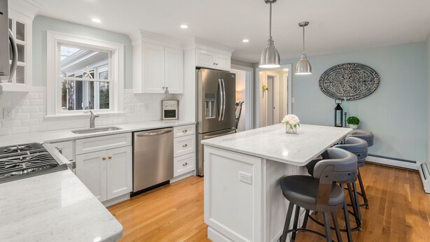 A modern kitchen with white cabinetry, stainless steel appliances, and a marble island with bar stools.
