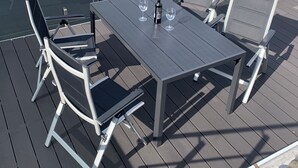 Une terrasse avec une table et quatre chaises, une bouteille et deux verres.