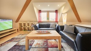 Un salon chaleureux avec un canapé en cuir noir, une table basse en bois et un téléviseur posé sur un meuble.