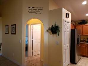 A hallway with a door leading to a bedroom, a kitchen area with a refrigerator, and a wall-mounted sign.