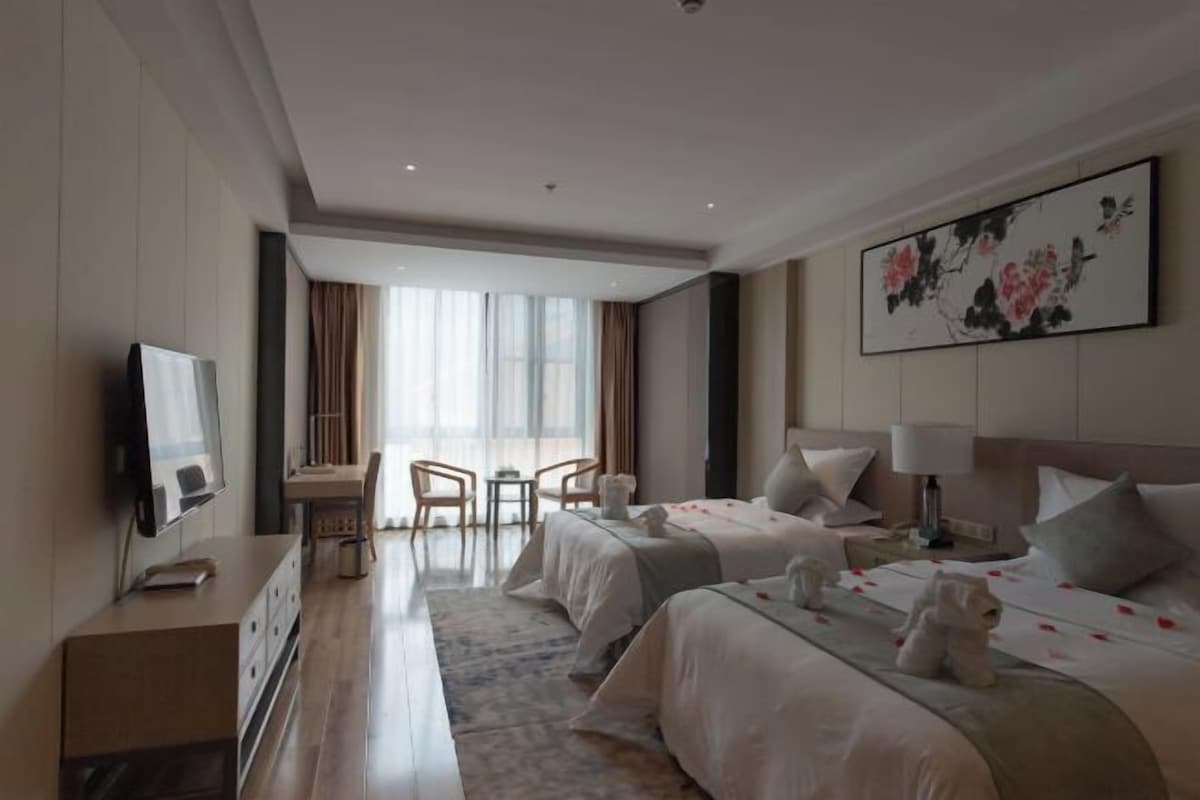 A hotel room with two beds, a desk, a television, and a large window.