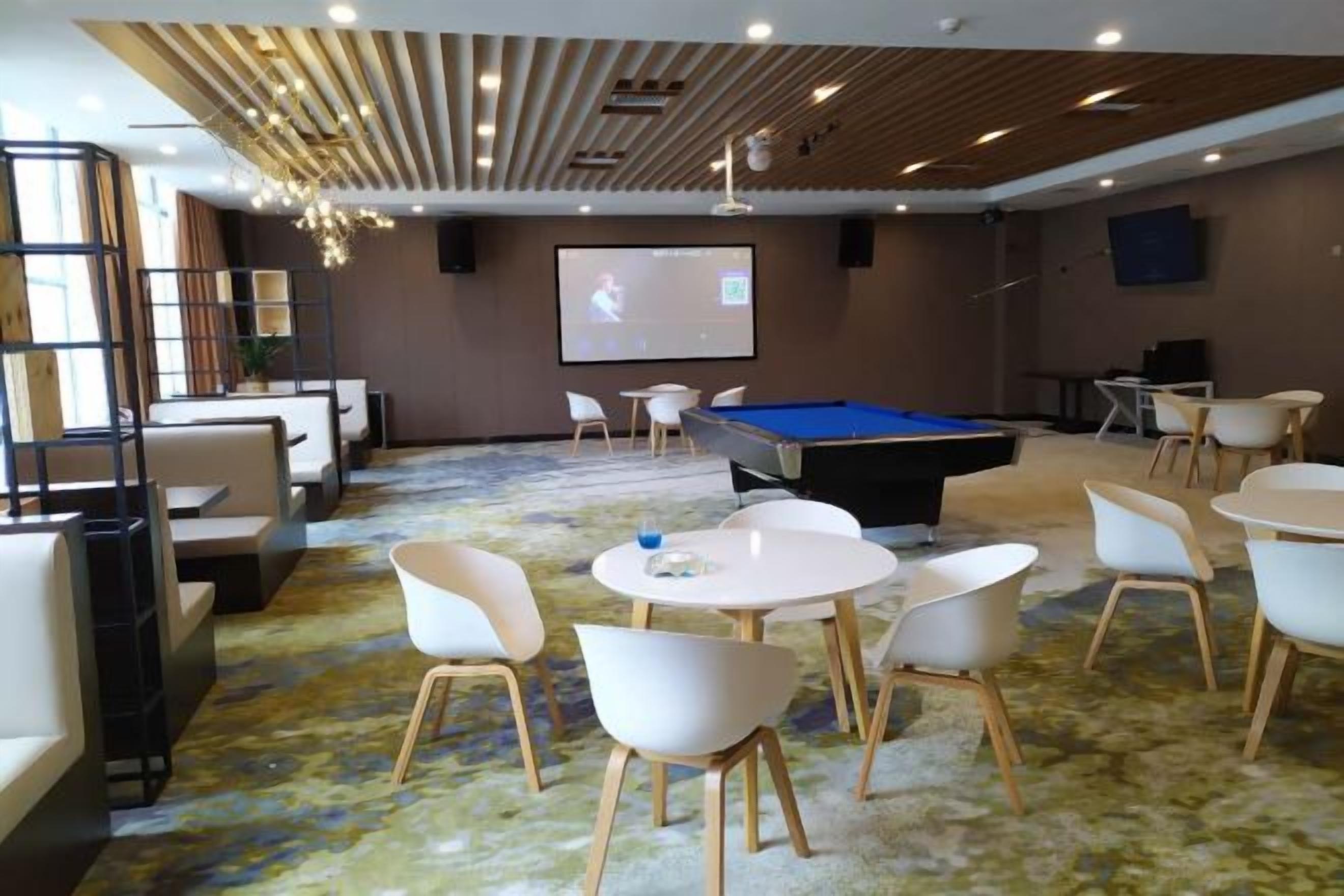 Una habitación con mesa de billar, sillas blancas, pantalla para proyector y piso alfombrado.