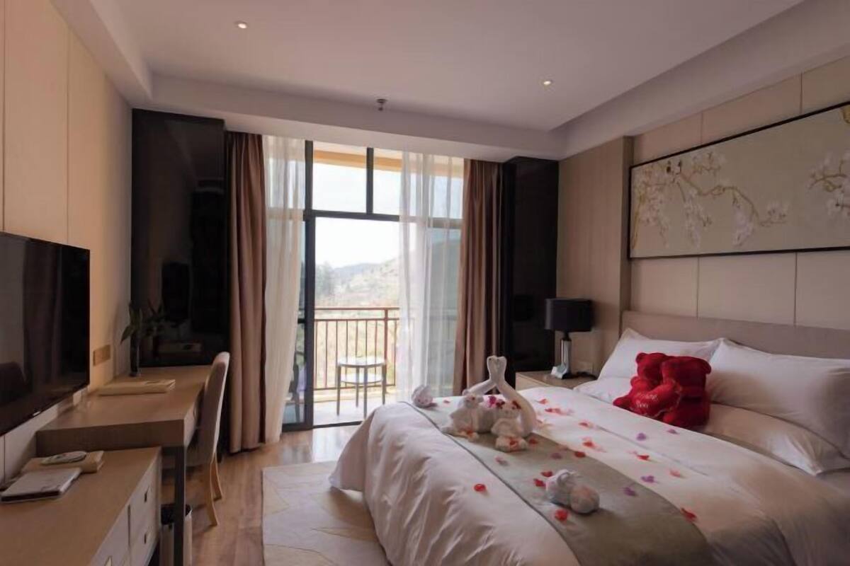 Une chambre d’hôtel avec un lit, un bureau, une télévision et un balcon offrant une vue.