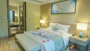 A hotel room with a bed, bedside tables, a mirror, a painting, and a bathroom visible through an open door.