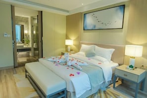 A hotel room with a bed, bedside tables, a mirror, a painting, and a bathroom visible through an open door.