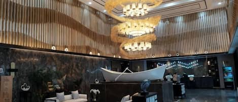 A modern lobby with a reception desk, seating area, and a large chandelier.
