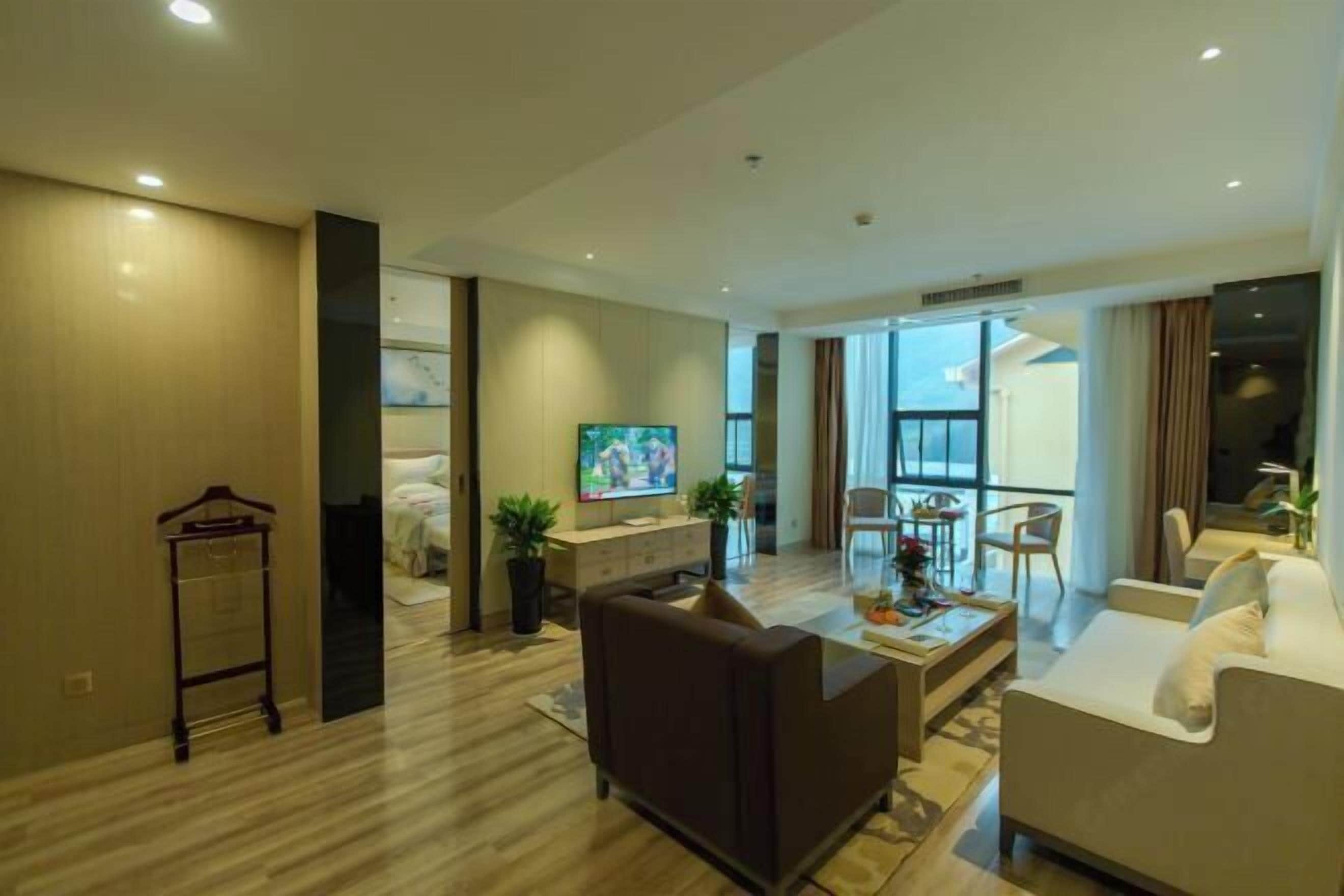Una sala de estar moderna con sofá, mesa de centro y televisor. Tiene piso de madera y vista al exterior a través de amplios ventanales.