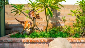 Eine Dinosaurier-Statue in einem angelegten Garten mit einer Ziegelmauer und viel Grün.