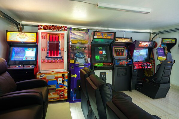 Une rangée de bornes d’arcade dans une pièce dont le sol est recouvert de carreaux et qui est éclairée par un luminaire au plafond.