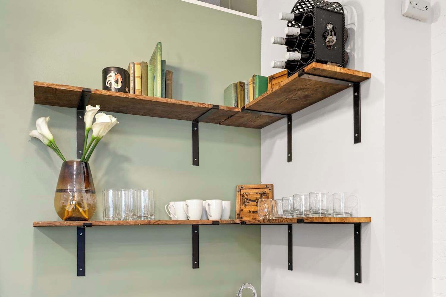 A wall-mounted shelf unit with books, a vase with flowers, and glasses.