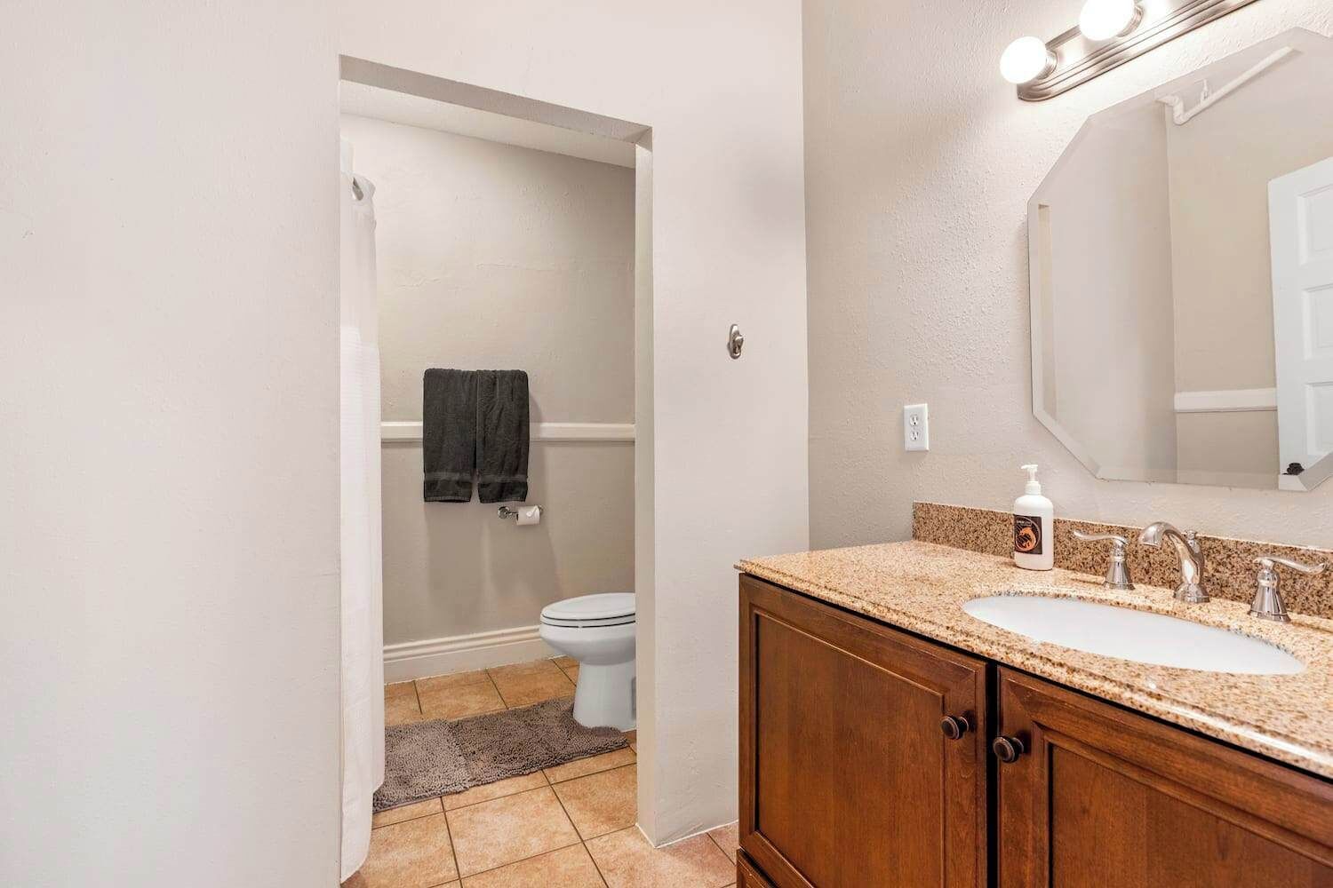 A bathroom with a white toilet, a wooden vanity with a granite countertop, and a large mirror above the sink.
